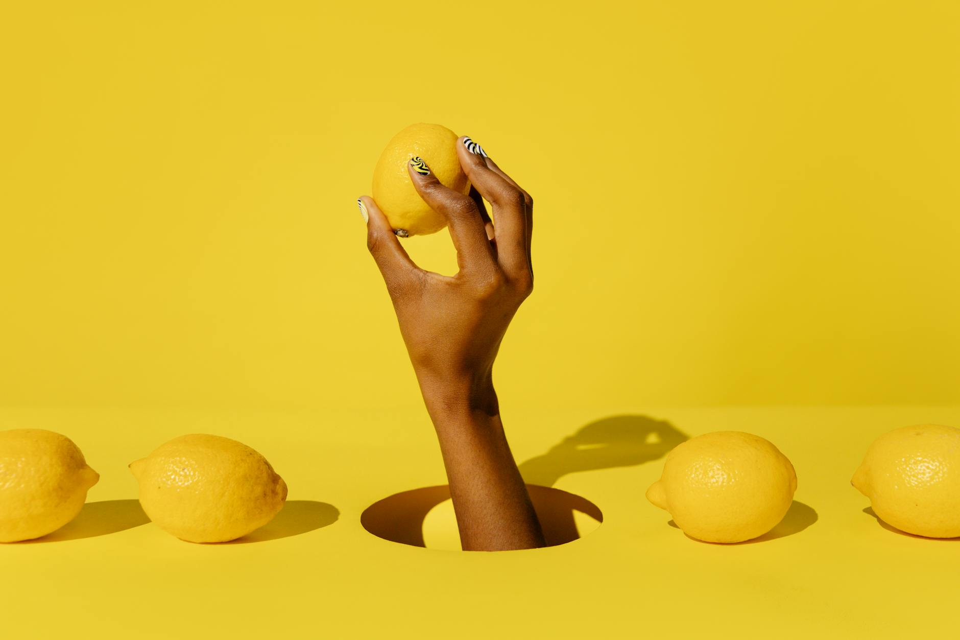 A hand holding a fresh lemon against a vivid yellow background, representing natural intimacy solutions
