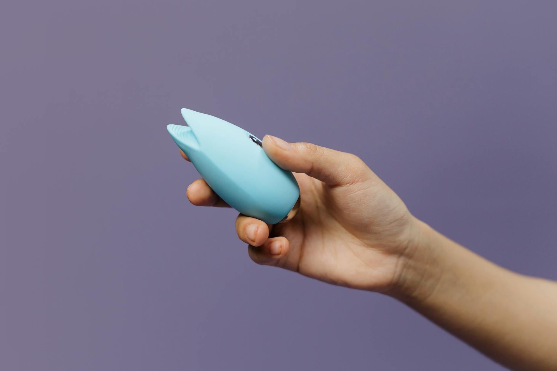 A hand holding a blue silicone vibrator against a purple background, representing safe self-pleasure