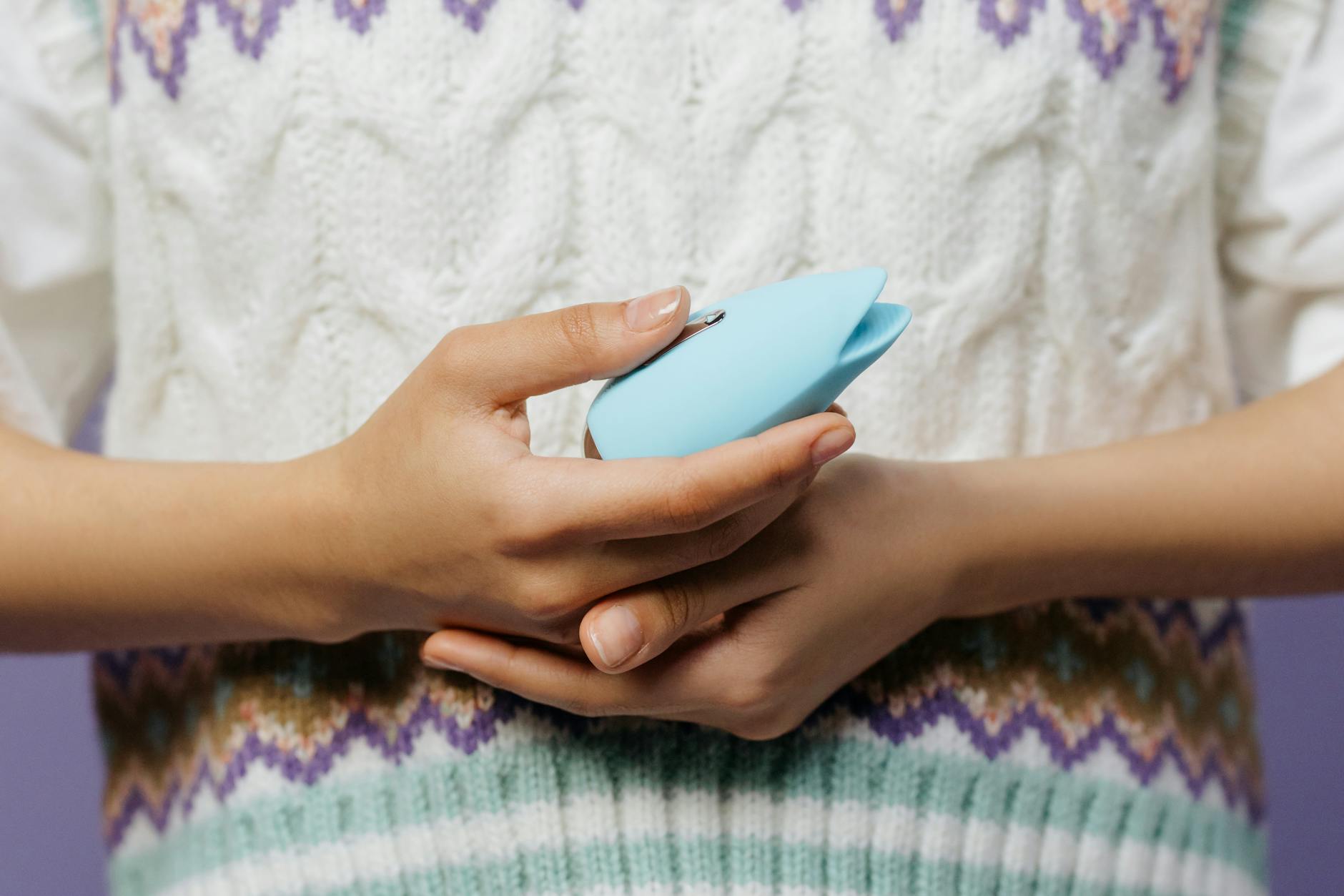 Hands holding a blue personal massager against a knitted sweater, representing reconnection with touch during grief.