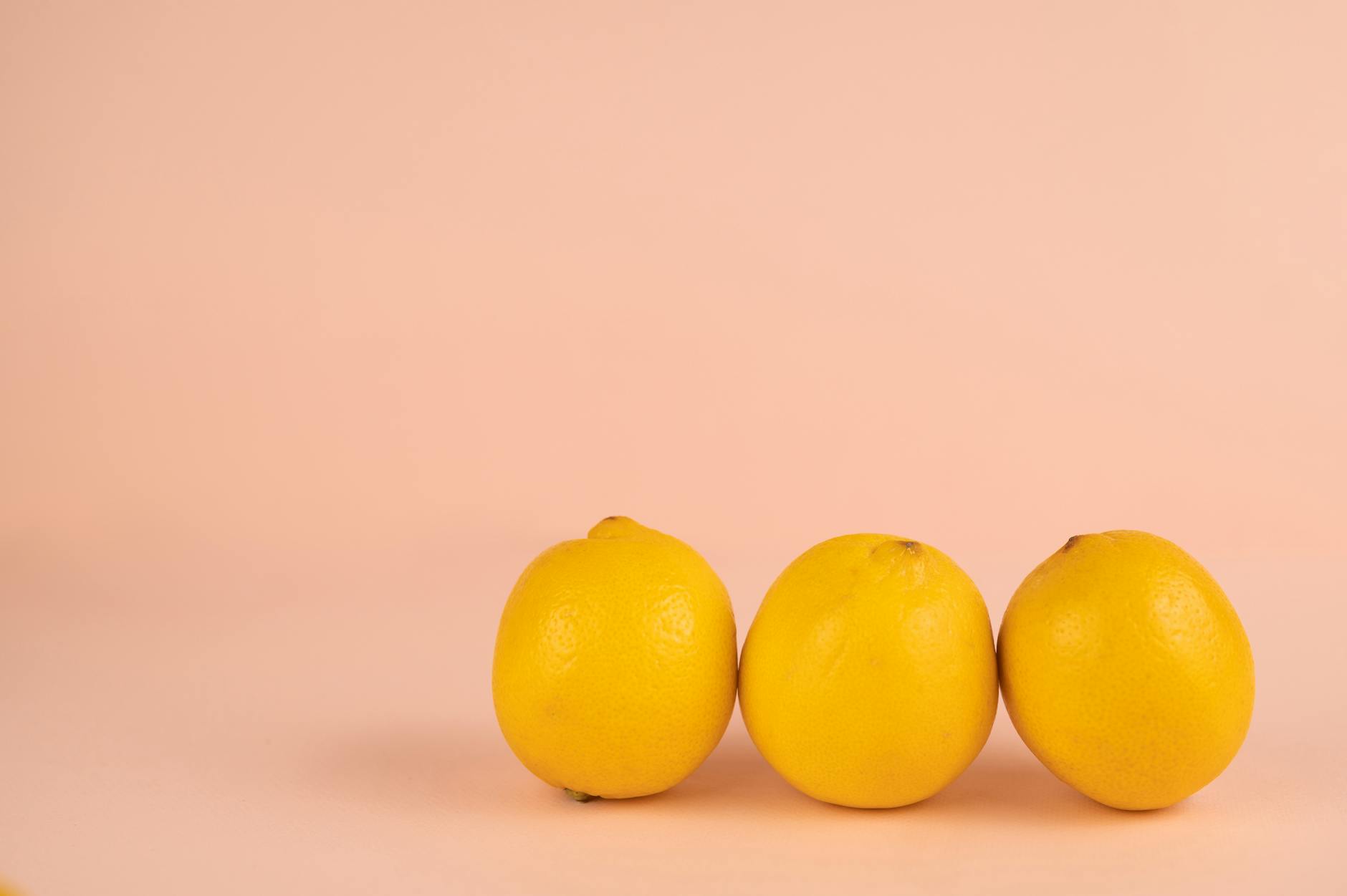 Two hands holding pink and blue silicone lemon vibrators against a pastel background